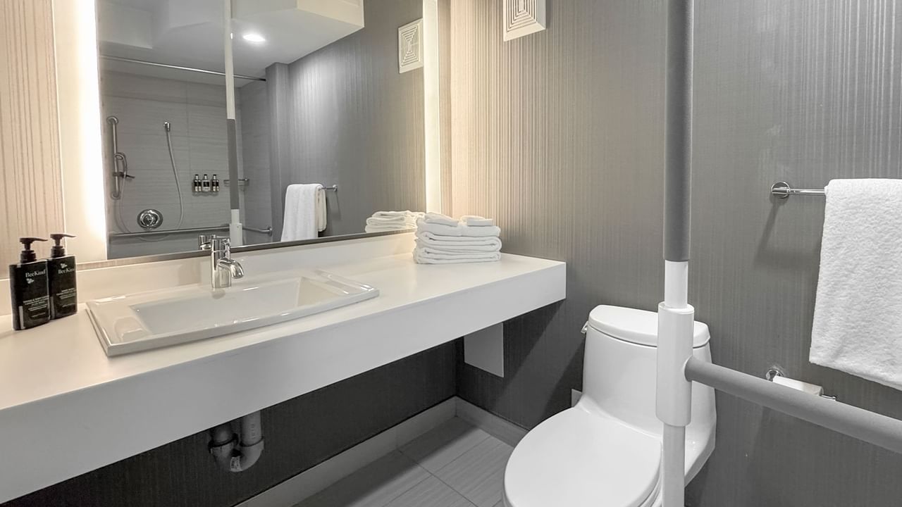 Accessible bathroom with a toilet, sink, mirror, white towels, and grab bars.