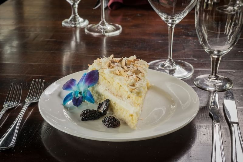 Slice of coconut layer cake served with blackberries and a blue orchid flower at Shangri-La Resort and Golf Club