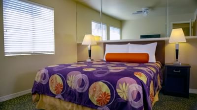 Guest room with purple patterned bedding, orange accent pillow, and bedside lamps at London Bridge Resort
