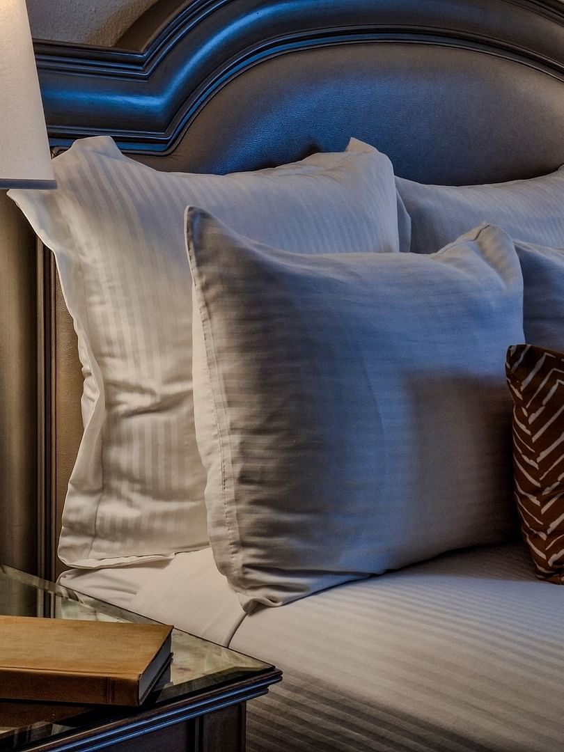 Glass lamp by a book on a nightstand under a padded headboard in Classic King Accessible at Warwick Melrose Dallas