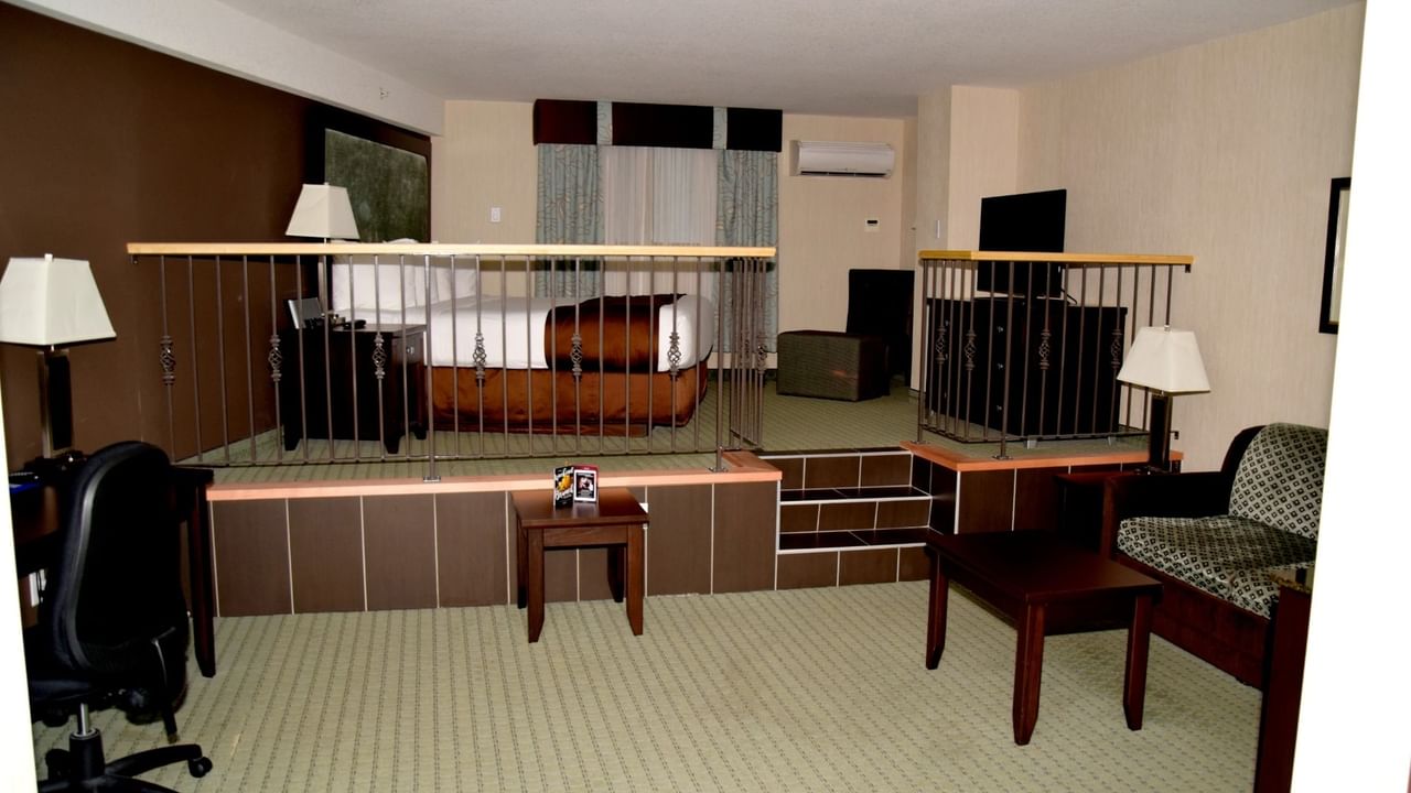 Hotel room with a raised bed area, desk, two lamps, and a seating area with a couch.