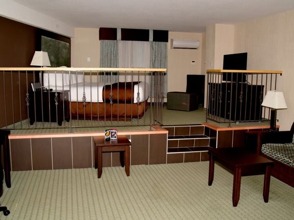 Hotel room with elevated bed area and living space with furniture.