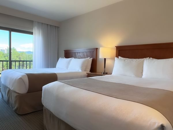 Guest room with two queen beds, balcony chair and desk