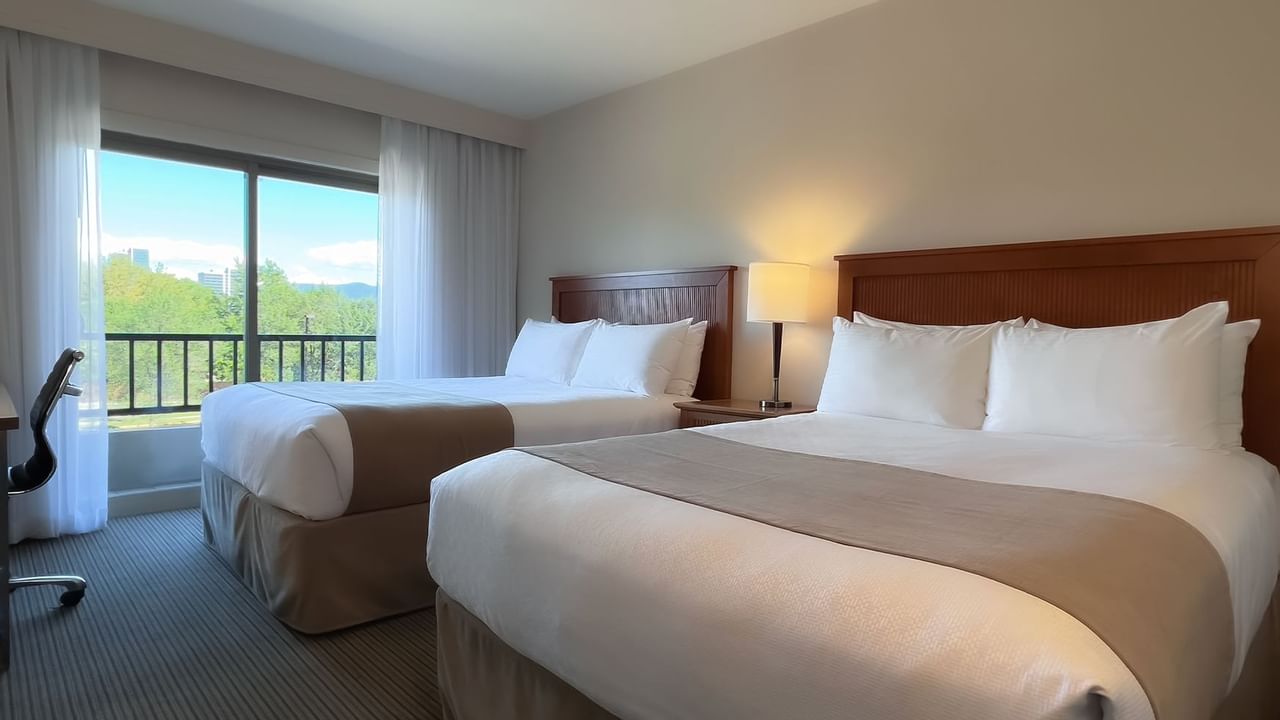 Guest room with two queen beds, balcony chair and desk