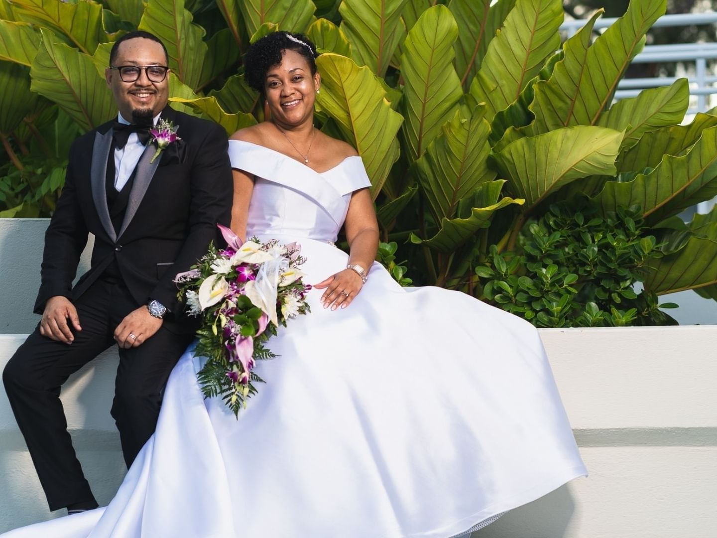 Smiling newlyweds pose for a photo by lush greenery at Savannah Beach Hotel.