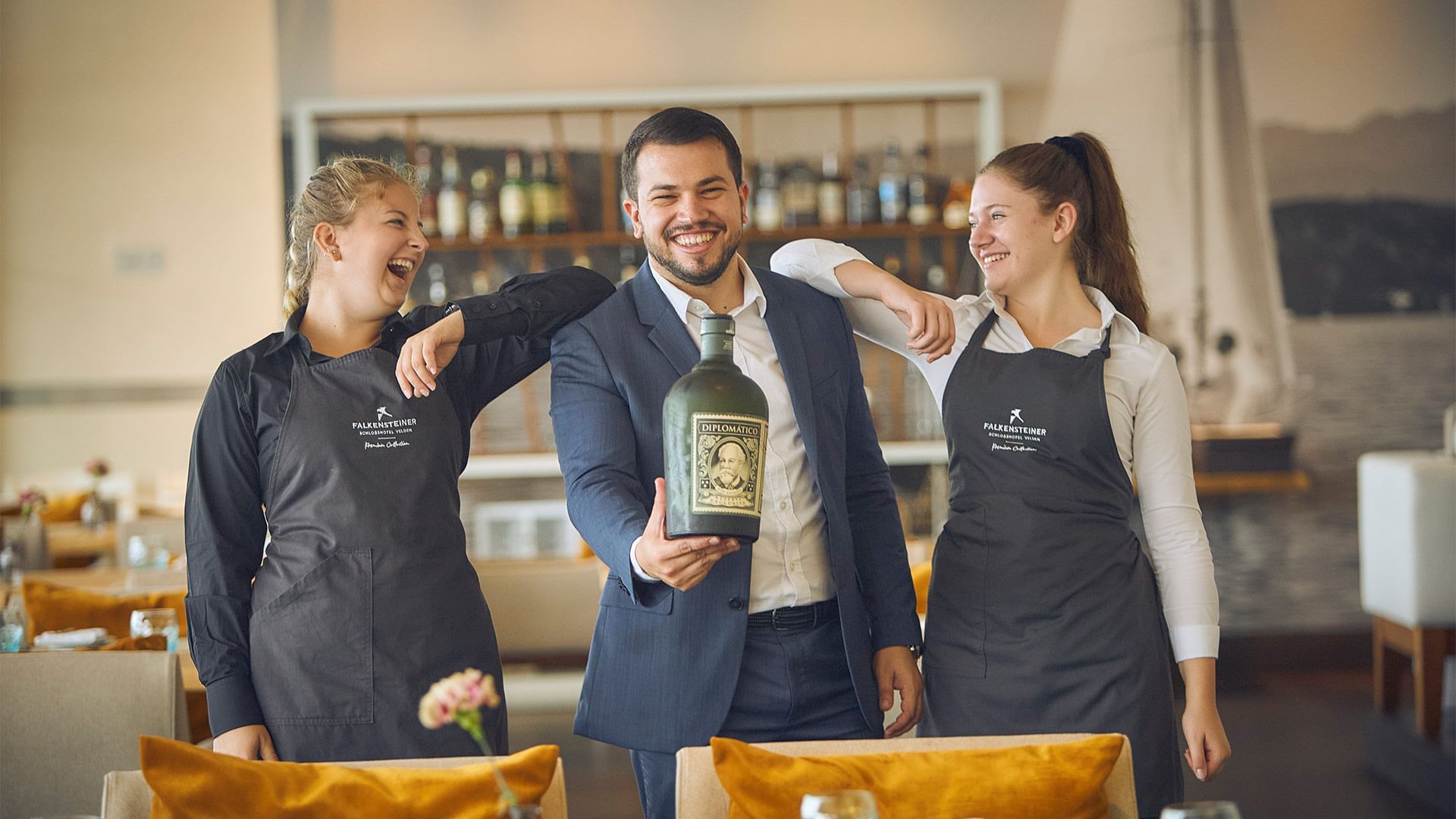 Two people in aprons standing with a man with a wine bottle at Falkensteiner Hotels & Residences