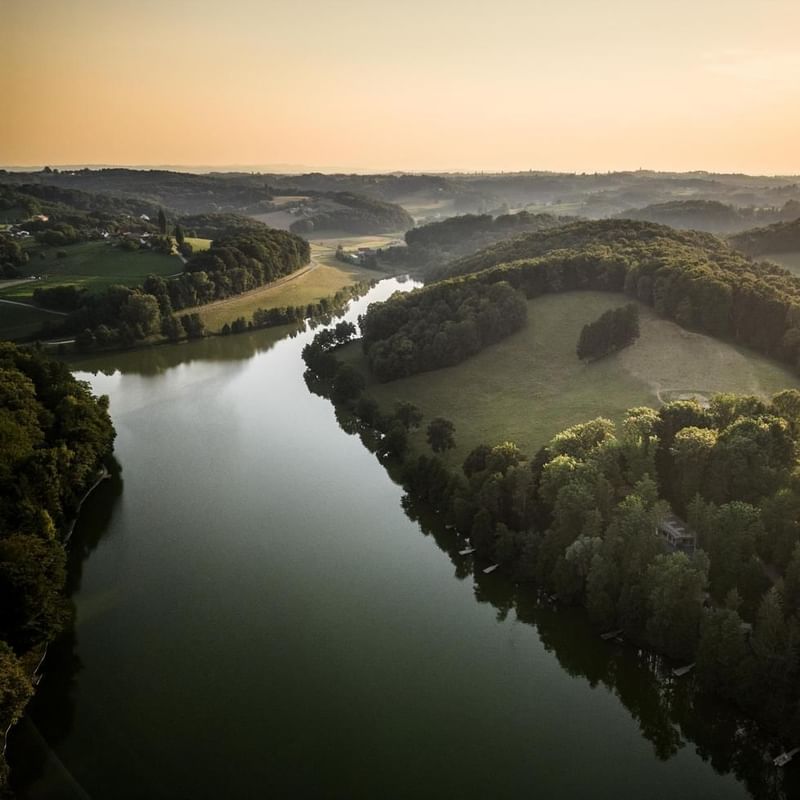 Luftaufnahme eines Flusses umgeben von grünen Feldern und Wäldern bei Sonnenuntergang.
