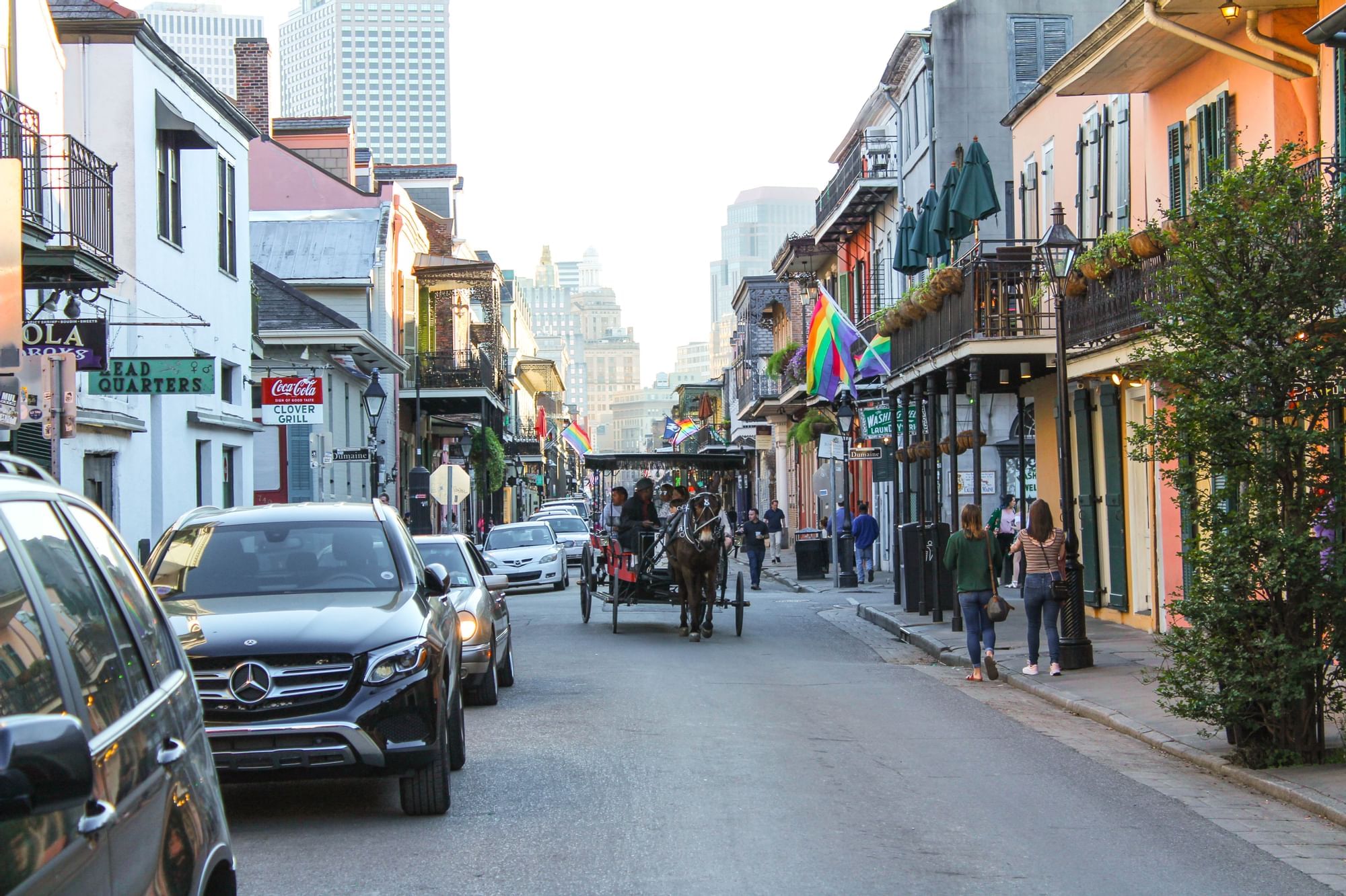 A street scene in a city with a horse-drawn carriage, cars, and people.