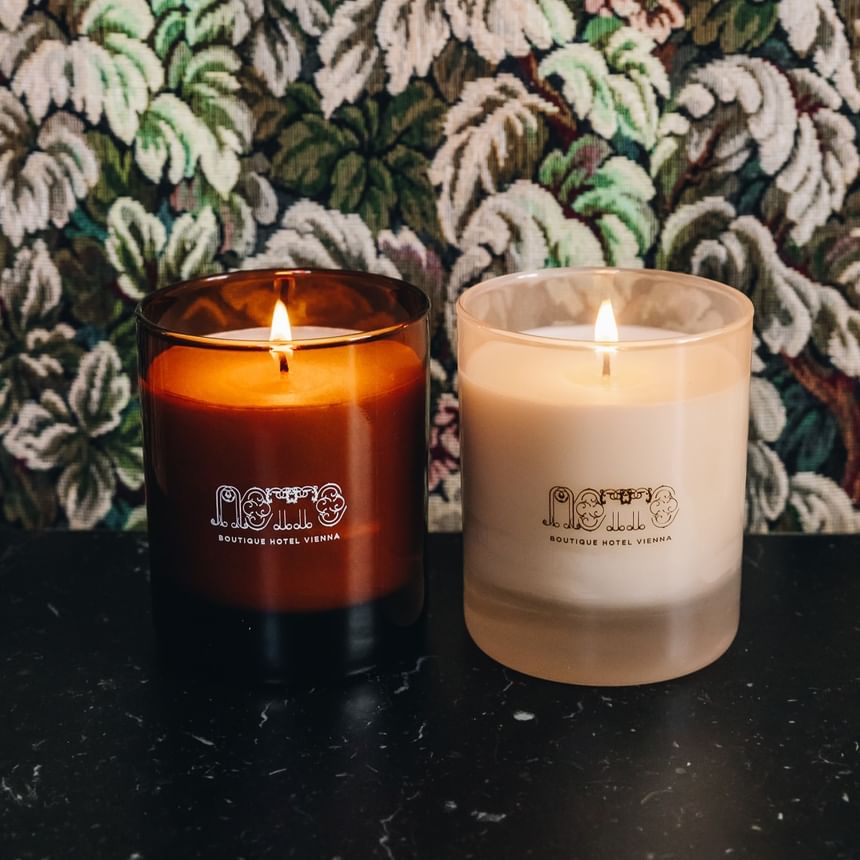 Zwei brennende Kerzen von Hotel Motto vor einer floralen Tapete bei Hotel Motto