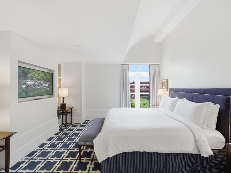 Deluxe King Suite with white bedding, navy upholstered headboard, and wall-mounted TV at el PRADO Hotel, Palo Alto.