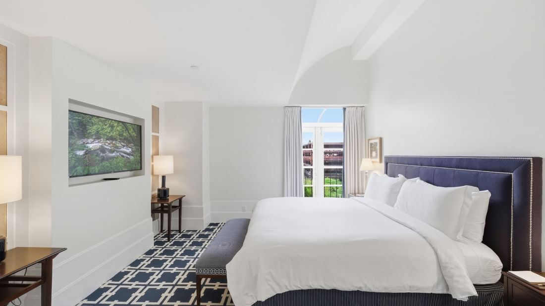 Deluxe King Suite with white bedding, navy upholstered headboard, and wall-mounted TV at el PRADO Hotel, Palo Alto.