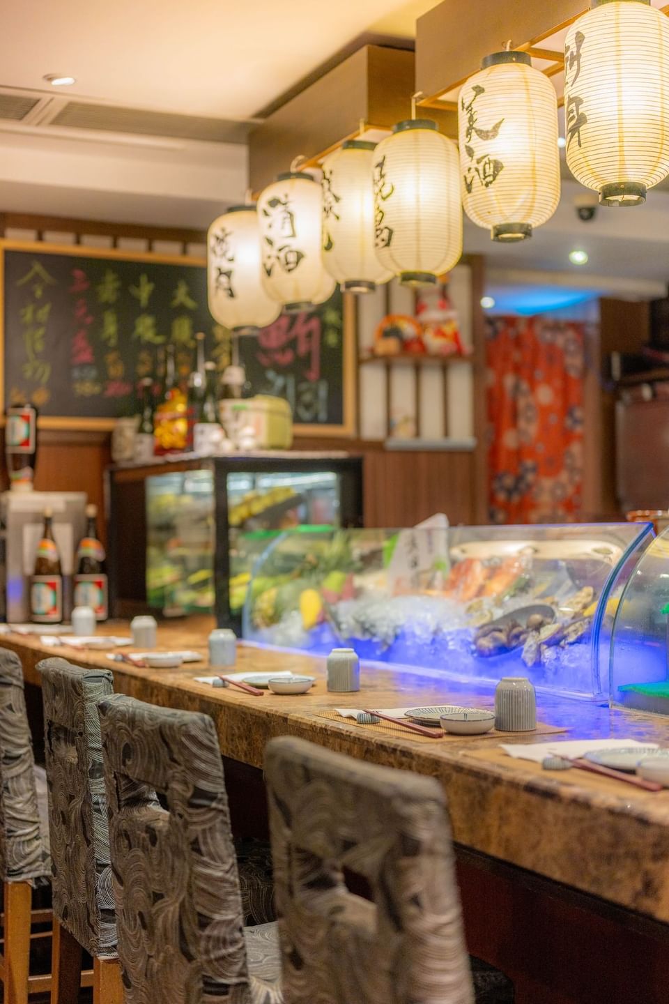 Interior of Royal Robatayaki with hanging lanterns, a sushi bar, and colorful food displayed on ice under blue lighting