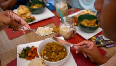 Close-up of person holding fork with rice beside a chicken curry dish in Hott Pott Restaurant at Worthing Court Apartment