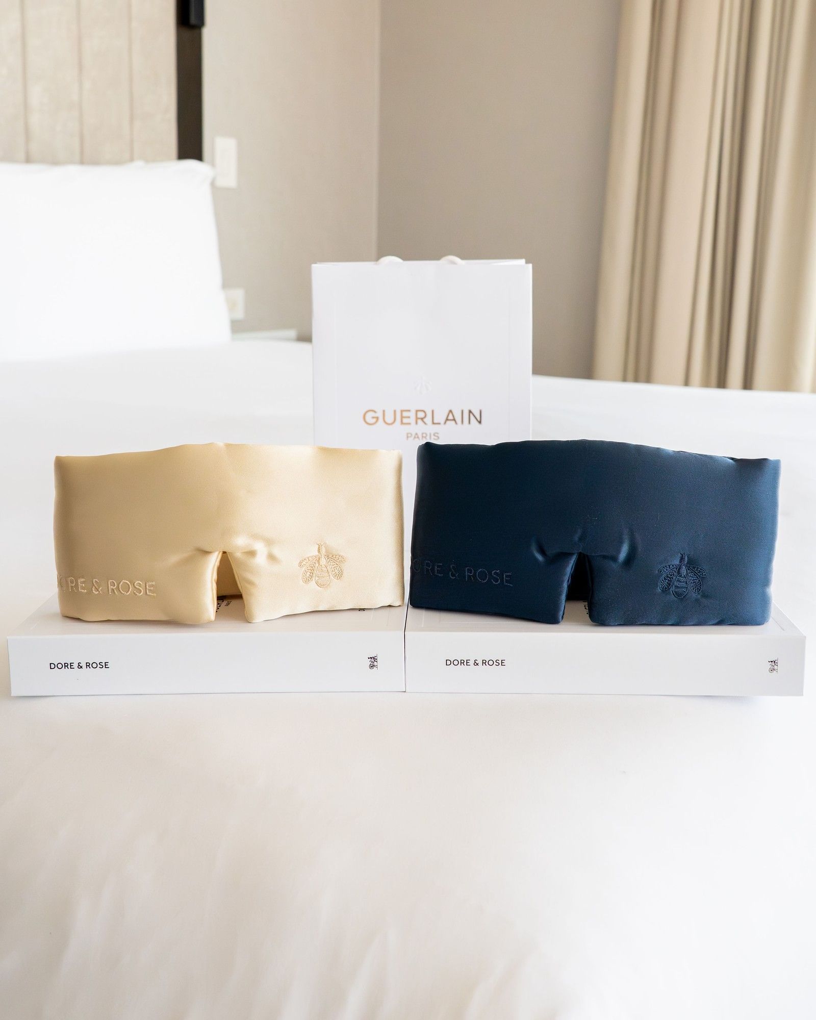 Guerlain Paris gift bag placed by two embroidered silk pouches, sitting atop soft white bedding at Hotel X Toronto
