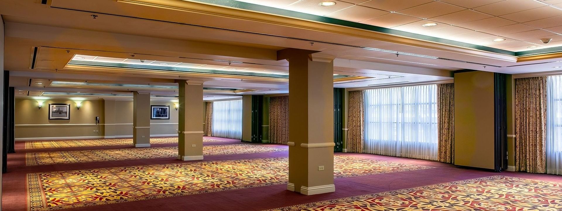 Large empty ballroom by tan pillars under bright lights on a patterned rug in Capitol Ballroom at Warwick Denver