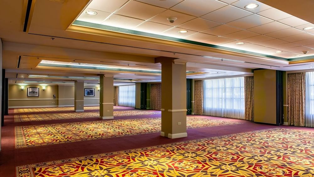 Large empty ballroom by tan pillars under bright lights on a patterned rug in Capitol Ballroom at Warwick Denver