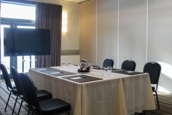 Black chairs by a long conference table under a wall light, with divider panels in a room at Rodd Miramichi River