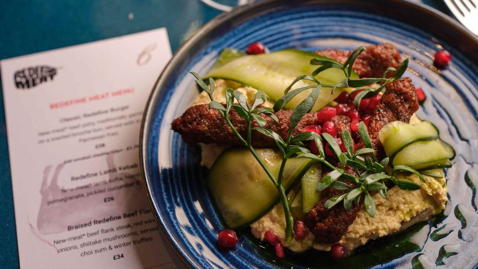 Lamb kebab on hummus by cucumber and pomegranate seeds in a blue bowl at Warwick Hotels & Resort