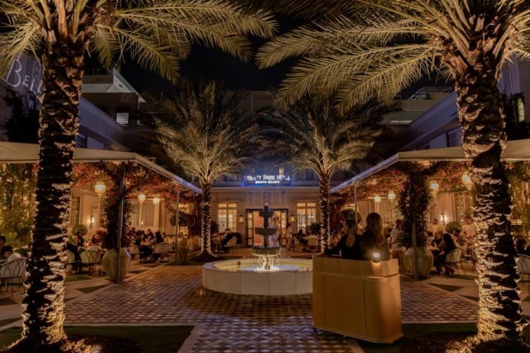 A nighttime view of a hotel courtyard with palm trees, a fountain, and a seating area.