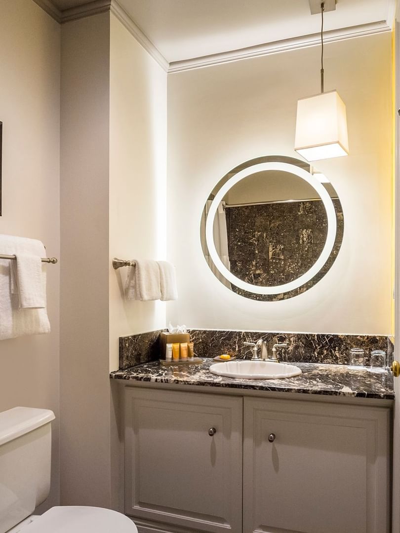 Backlit round mirror by a marble vanity under a pendant lamp in Balcony Suite at Warwick San Francisco