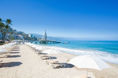 Beige lounge chairs on beach with pier view at Playa Los Arcos