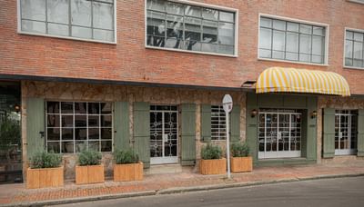 Brick exterior with green shutters by wooden planters under a yellow awning at 5Q House Chapinero