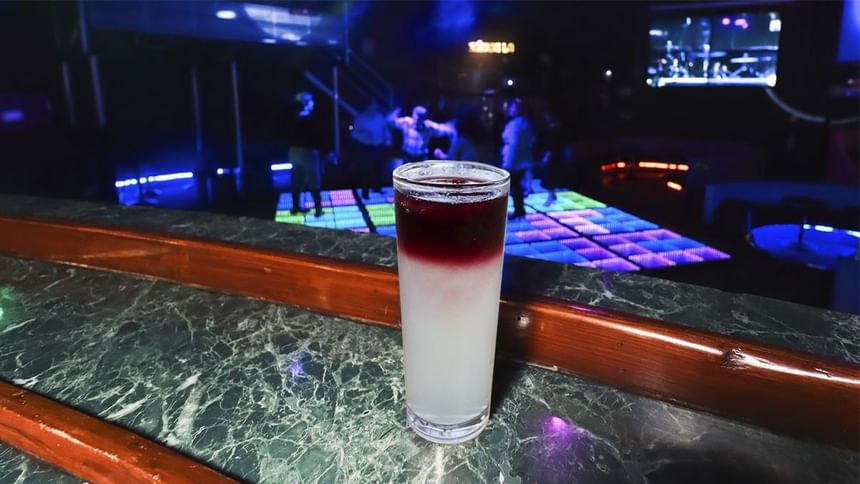Cóctel rojo y blanco en capas sobre barra de mármol con pista de baile iluminada al fondo en El Rollo de Araiza Palmira