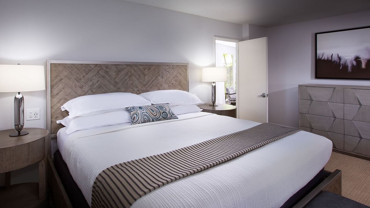 A hotel room with a large bed, nightstands with lamps, a dresser, and a painting on the wall.