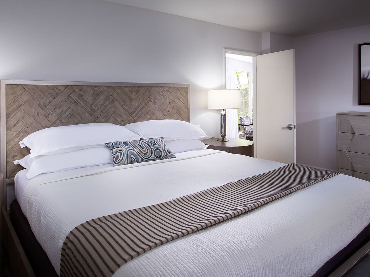 Bedroom with large bed, two lamps, and geometric dresser under a framed picture.