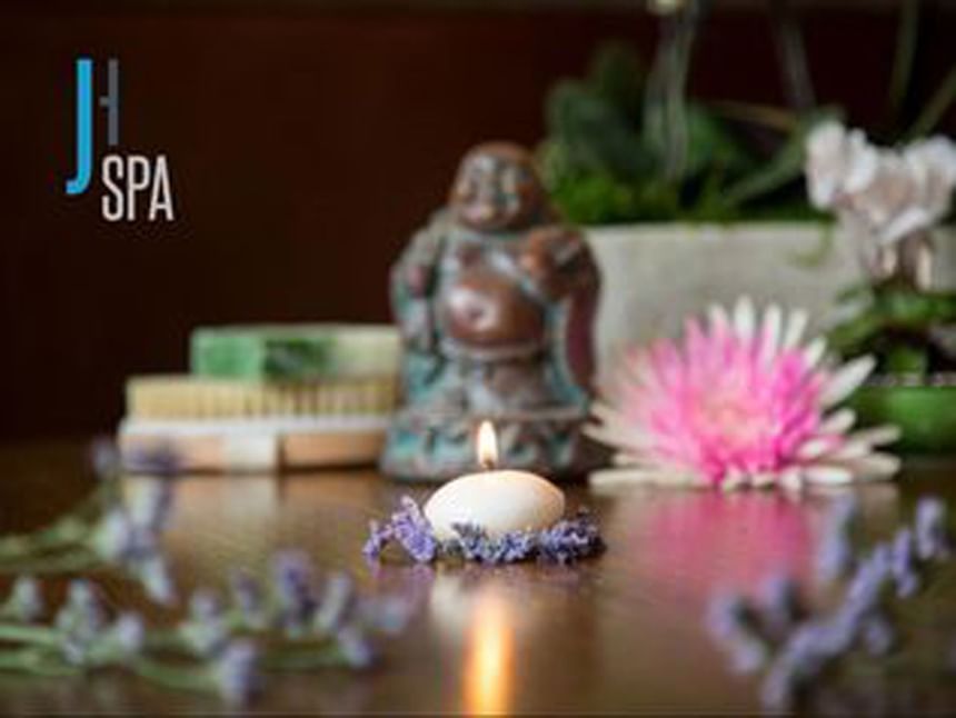 Small Buddha statue by a lit candle and pink flower under soft light in the J House Spa at The J House Greenwich