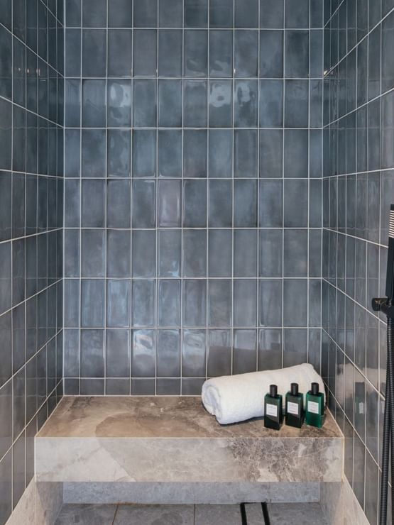 Elysium Two Bedroom Suite at Elysium Hotels with rolled towels and amenities by a stone bench in the tiled rain shower