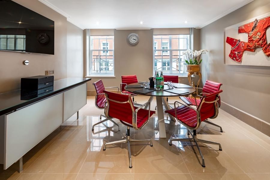 Round table with red leather armchairs for a meeting in a private suite at The May Fair Hotel