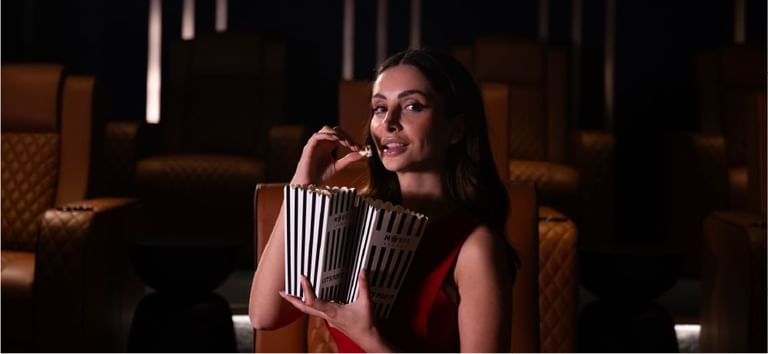 Woman savoring popcorn while seated in luxurious chairs at the exclusive The Movie Lounge inside DAMAC Maison Aykon City