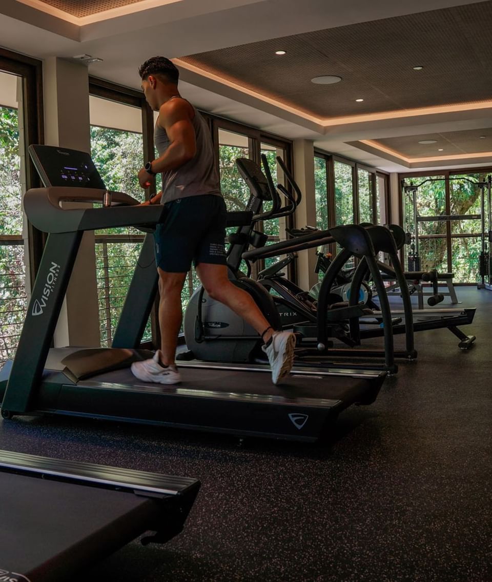 Man exercising on a treadmill in gym area with a greenery view at El Silencio Lodge & Spa