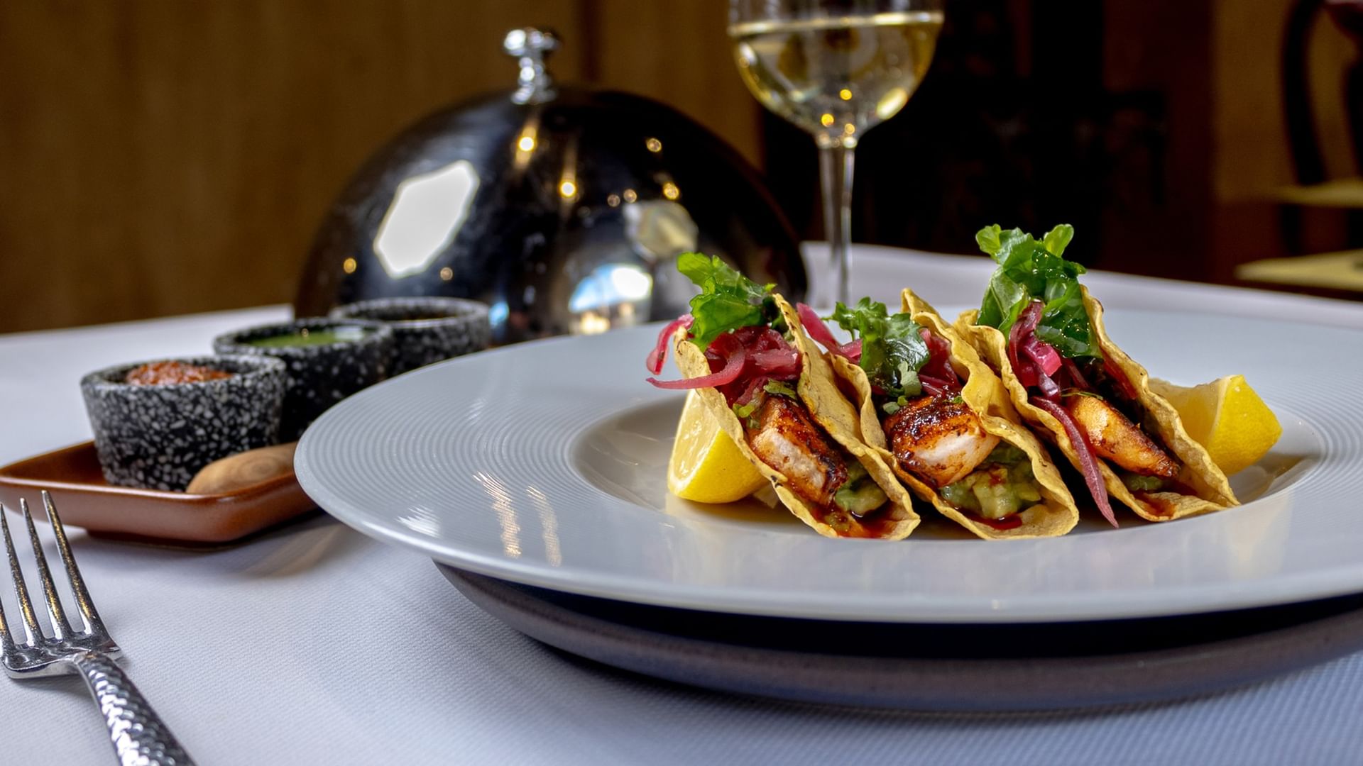 Three gourmet fish tacos served on a white plate with lemon and wine glass at Quinta Real Oaxaca