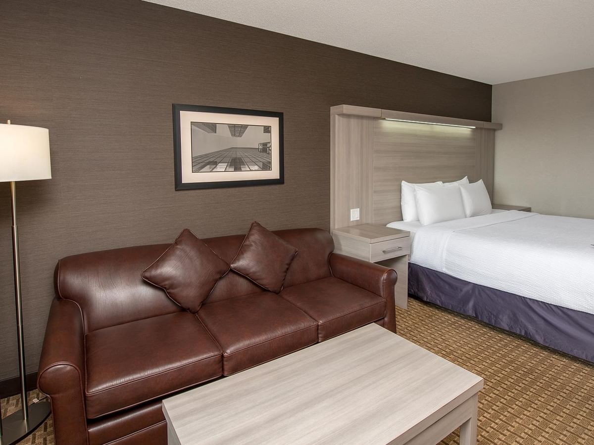 Coast Premium King room with king bed, brown leather sofa, and floor lamp at Coast Calgary University Area Hotel by APA.