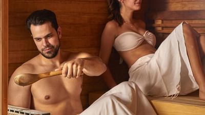 Couple dans un sauna en bois, avec un homme tenant une louche et une femme souriante.