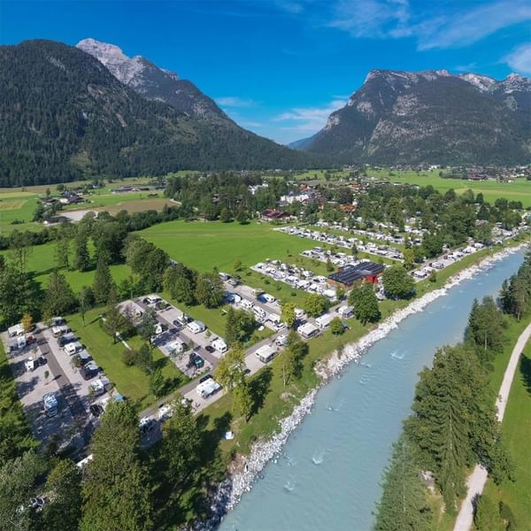 Luftaufnahme eines Campingplatzes neben einem Fluss, umgeben von grünen Feldern und Bergen.