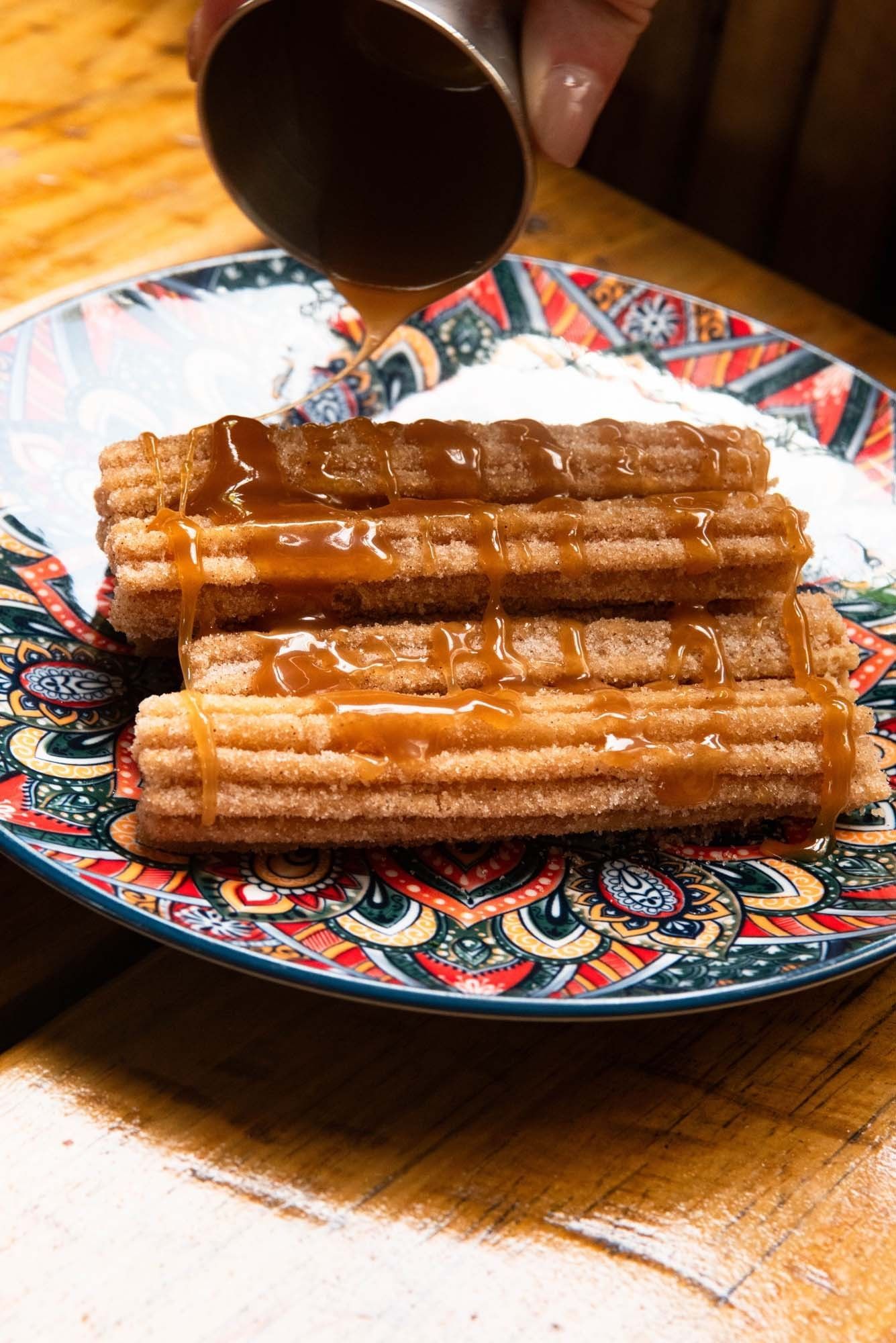A plate of churros being drizzled with caramel sauce