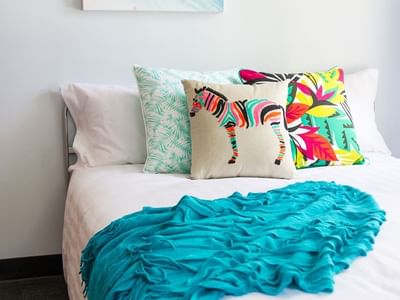 Bright bedroom with white bedding, colorful decorative pillows, turquoise throw, and abstract art at UniLodge on Margaret