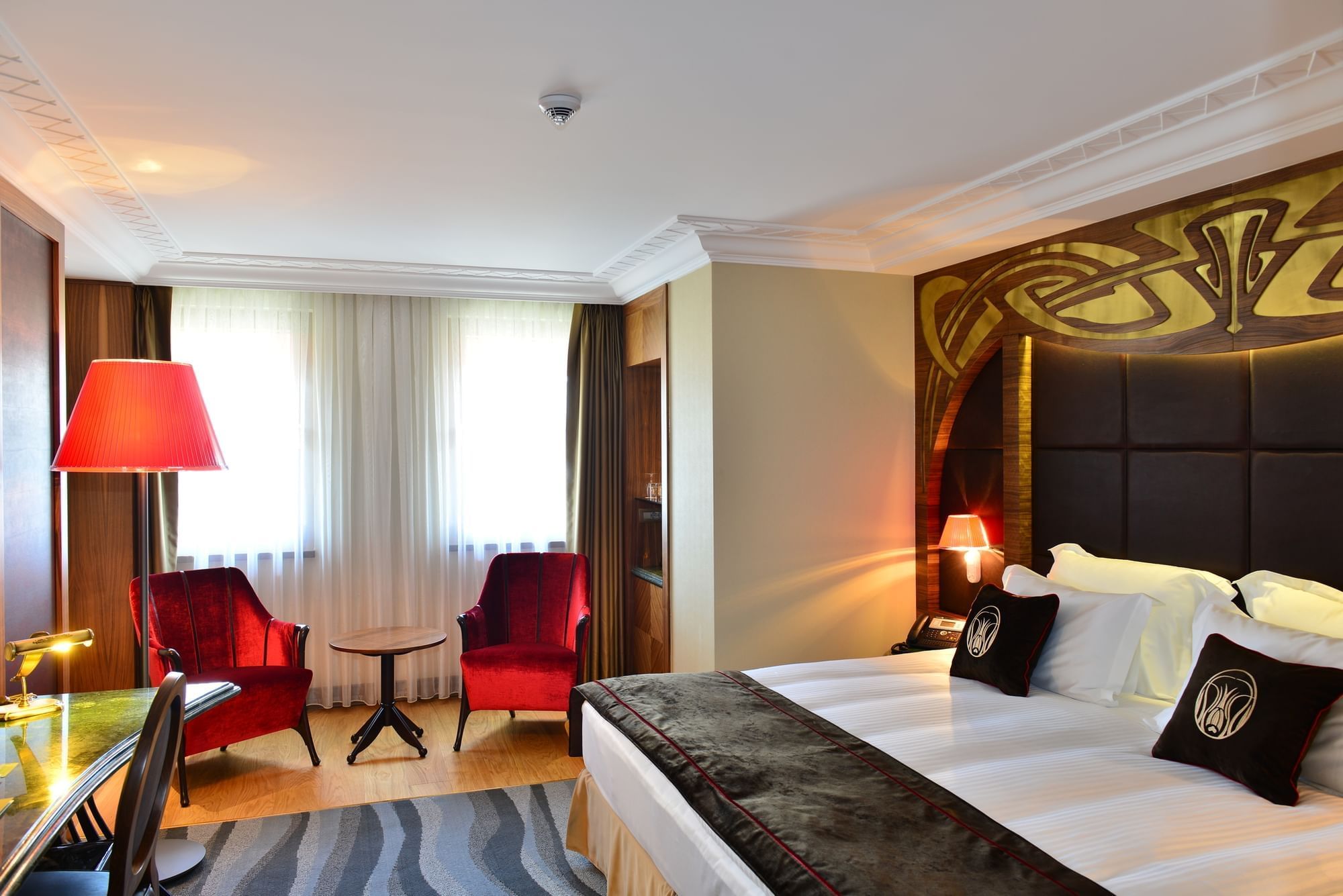 Red velvet chairs by a small table surrounding a bright window in Deluxe Room at Warwick Ankara