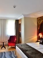 Red velvet chairs by a small table surrounding a bright window in Deluxe Room at Warwick Ankara