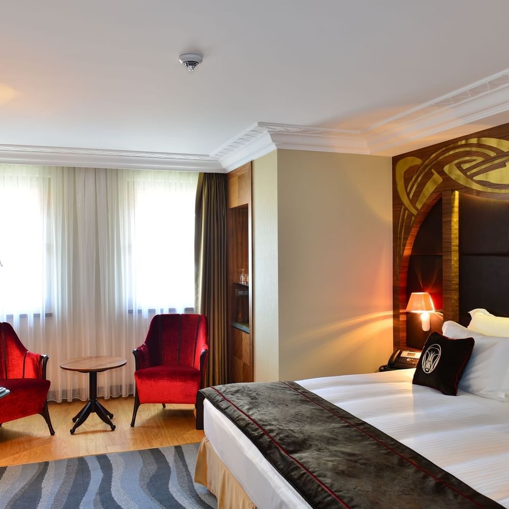 Red velvet chairs by a small table surrounding a bright window in Deluxe Room at Warwick Ankara