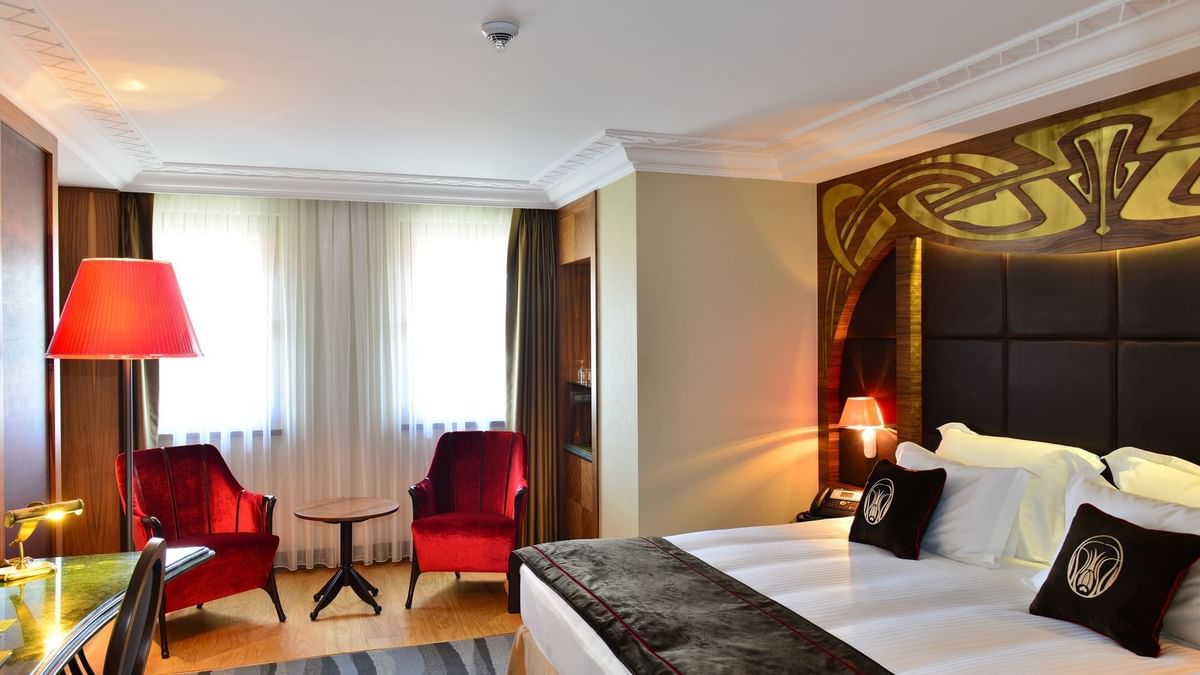 Red velvet chairs by a small table surrounding a bright window in Deluxe Room at Warwick Ankara