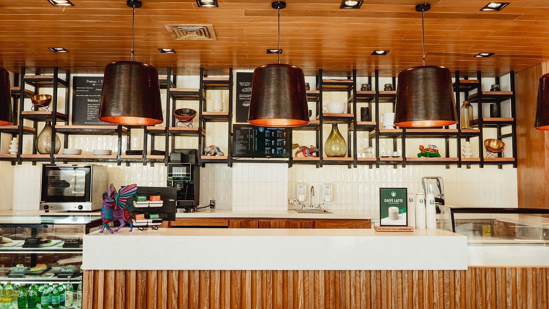 Warmly lit cafe counter with three large pendant lights overhead in Library Café & Deli at Camino Real Zaashila Huatulco