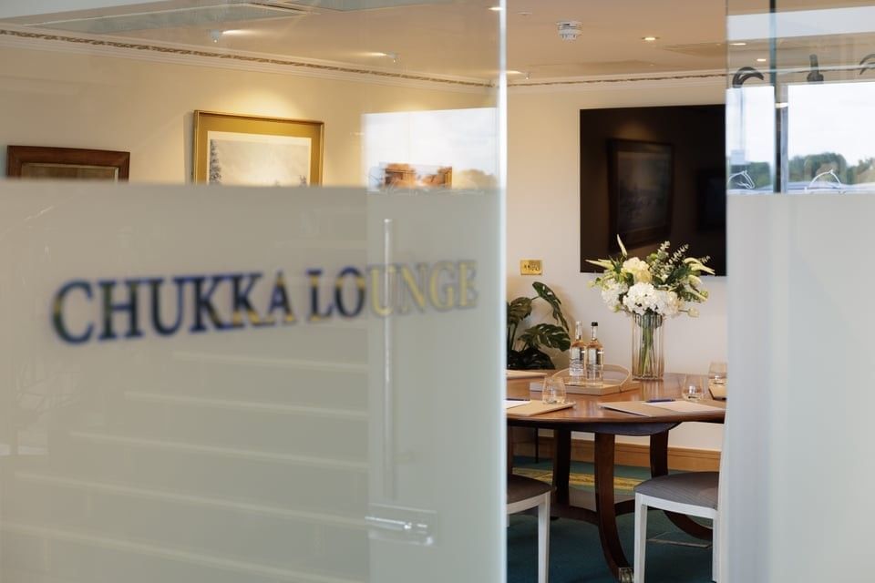 Glass door with Chukka Lounge gold lettering looking into a conference room with a large wooden table at the Polo Club Hotel