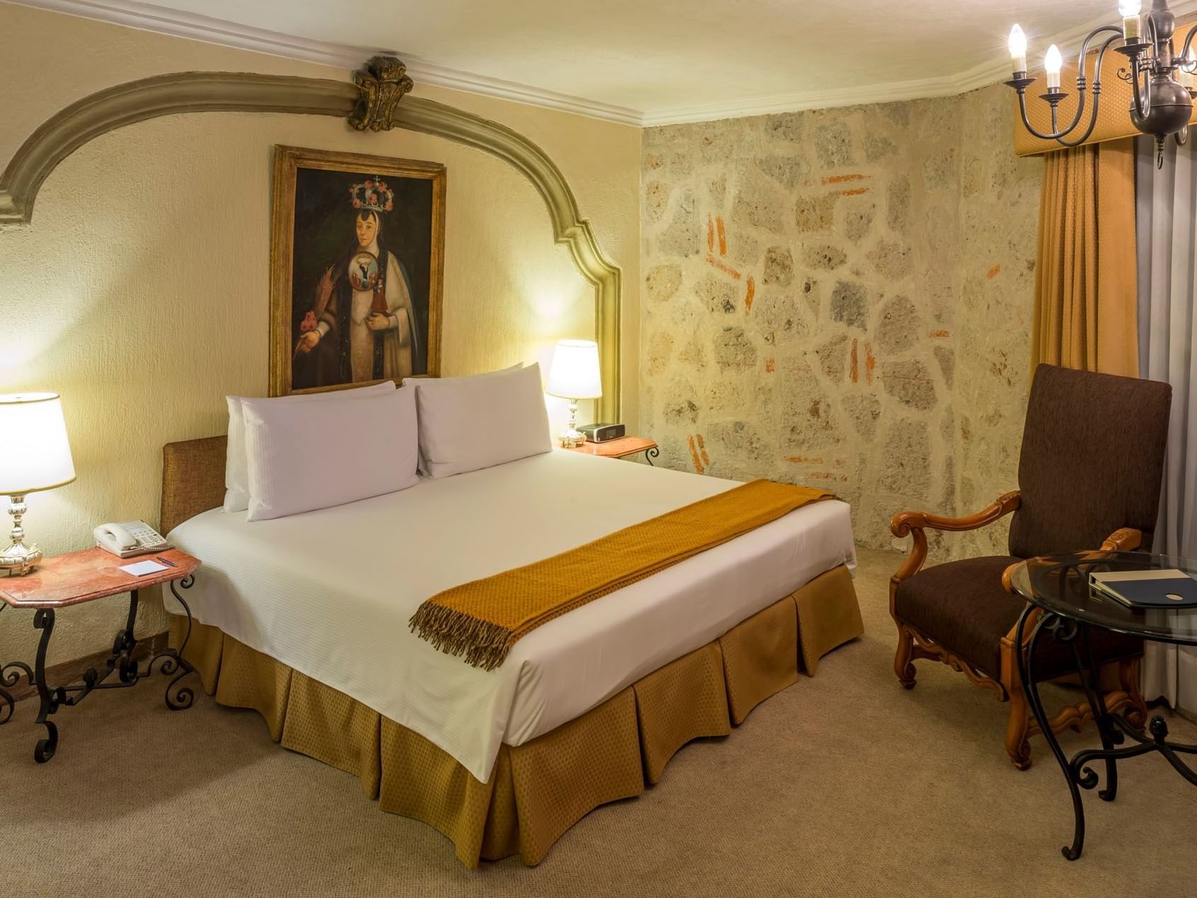 King Aguascalientes Suite with a stone accent wall, portrait art, and a plush chair at Quinta Real Aguascalientes