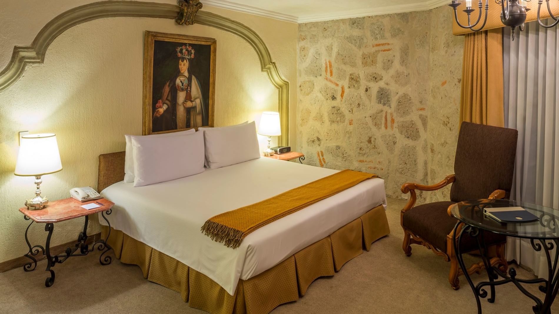 King Aguascalientes Suite with a stone accent wall, portrait art, and a plush chair at Quinta Real Aguascalientes