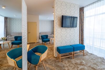 Living room with chairs, TV, patterned wallpaper, and large windows in Junior Suite at Metropol Hotel