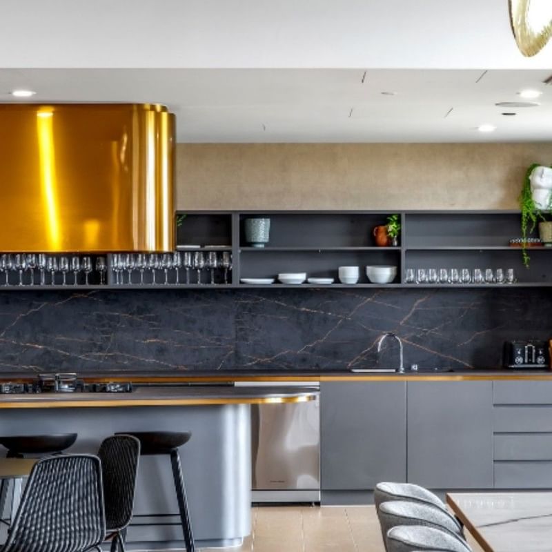 Modern kitchen with marble countertops, gold range hood, gray cabinets, dining area, and a plant on the wall.